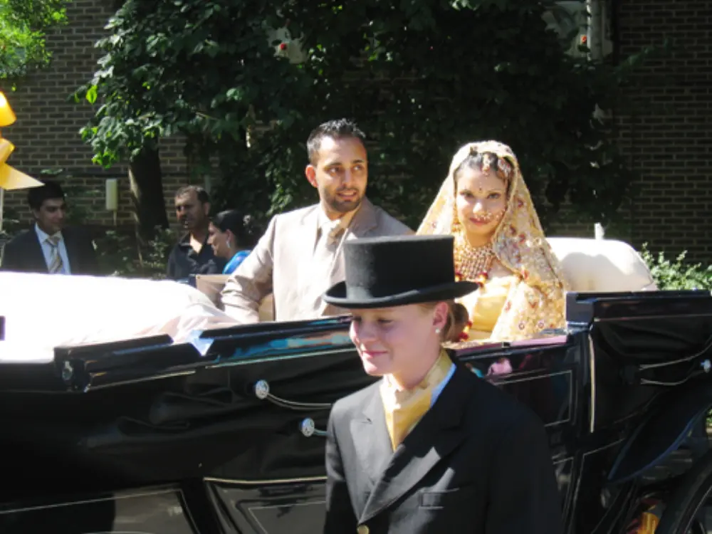 Asian bride and groom seated inside open-top black horse-drawn wedding carriage