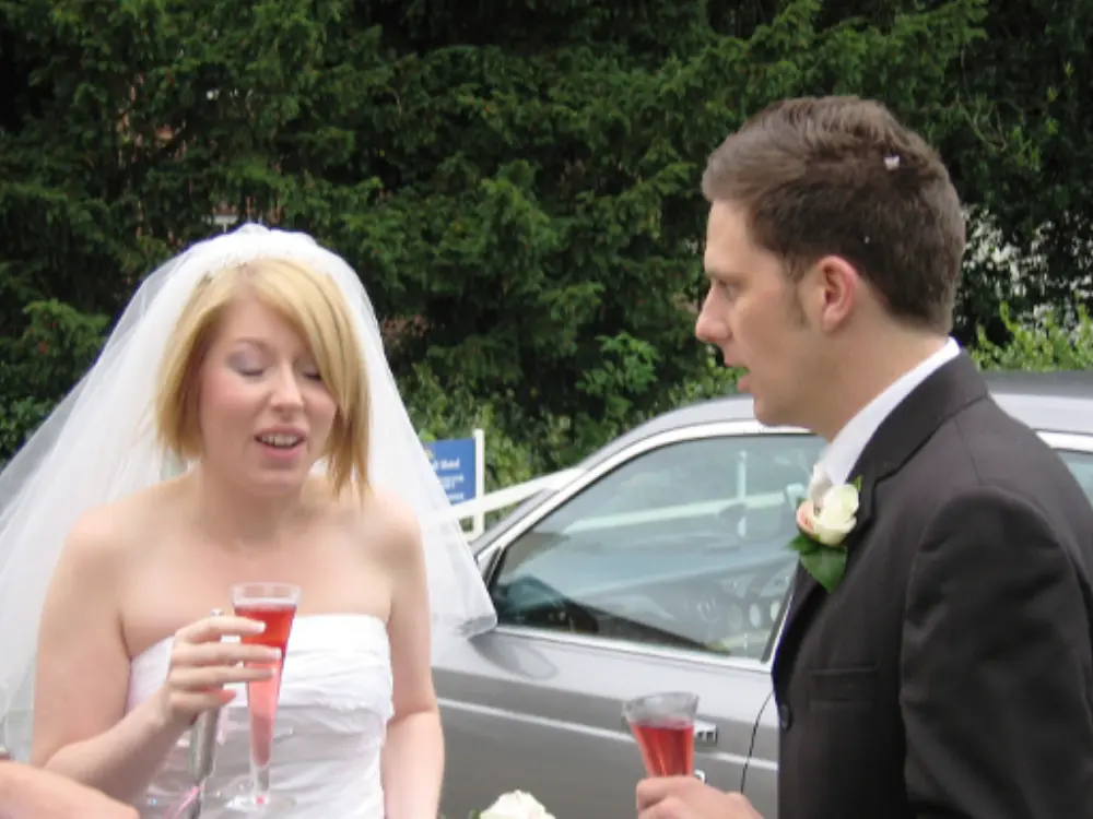 Bride and groom raising champagne flutes celebrating outside wedding car