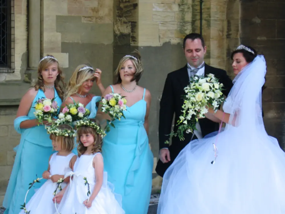 Bride and groom with bridesmaids in blue dresses admiring large wedding bouquet