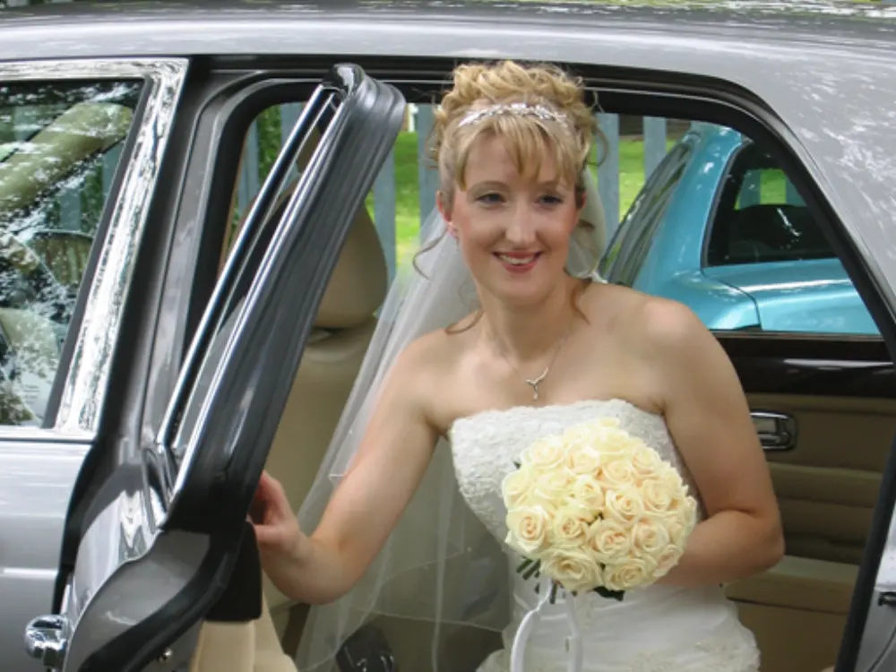 Blonde bride with cream rose bouquet stepping out of a silver Bentley wedding car