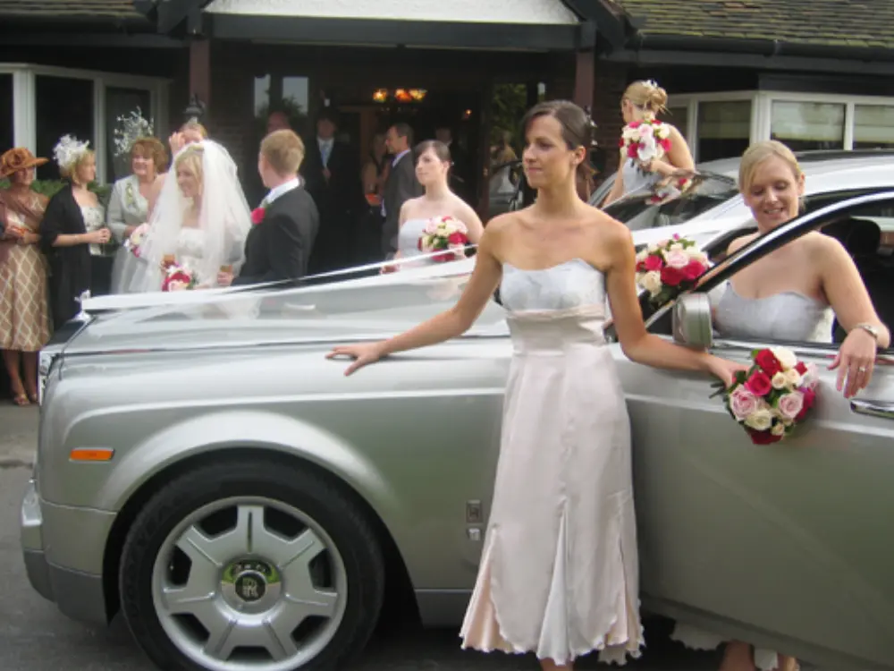 Bridesmaids in blush dresses posing alongside silver Rolls-Royce Phantom bridal car
