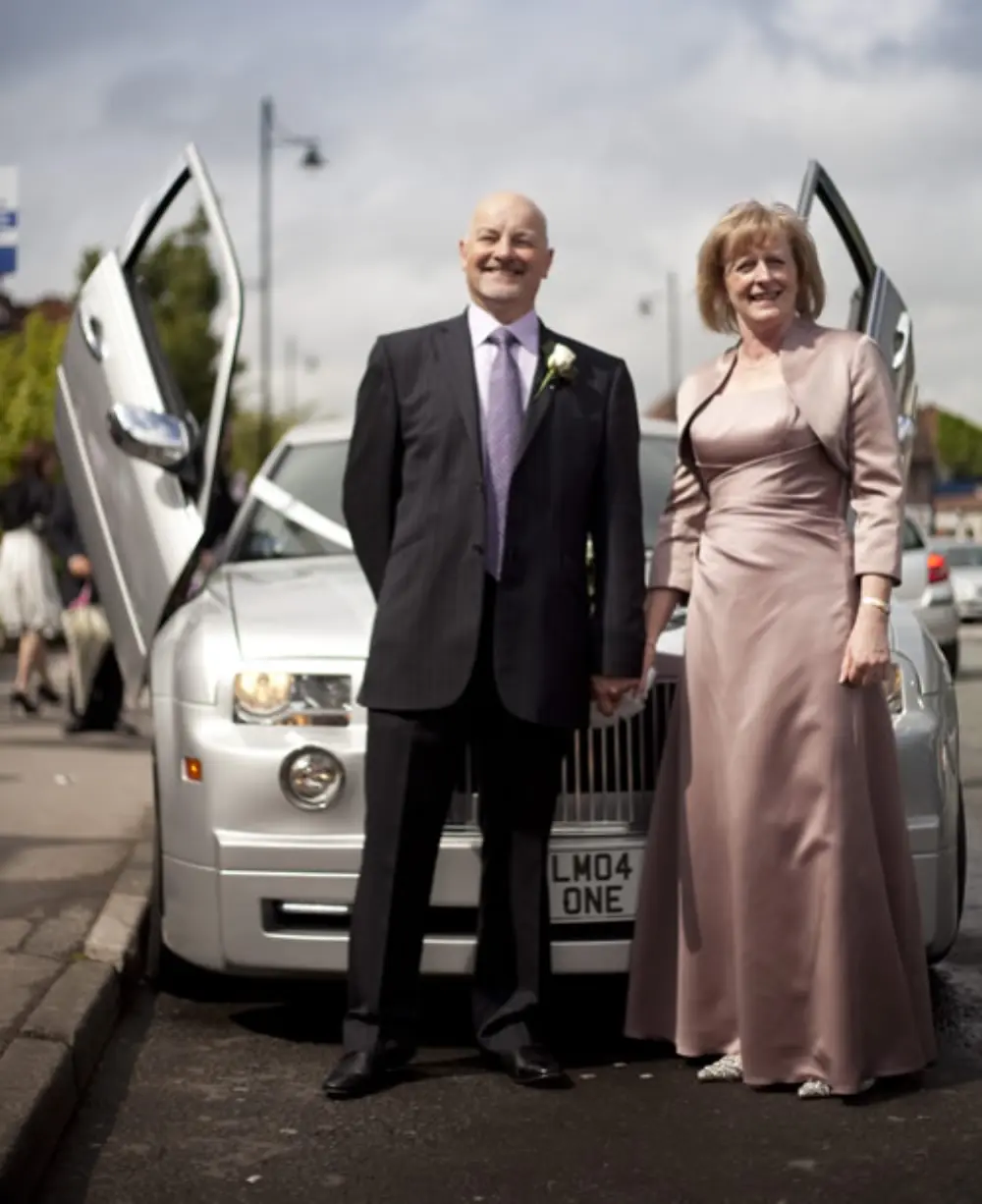 Couple holding hands in front of silver Chrysler limousine with gullwing scissor doors raised
