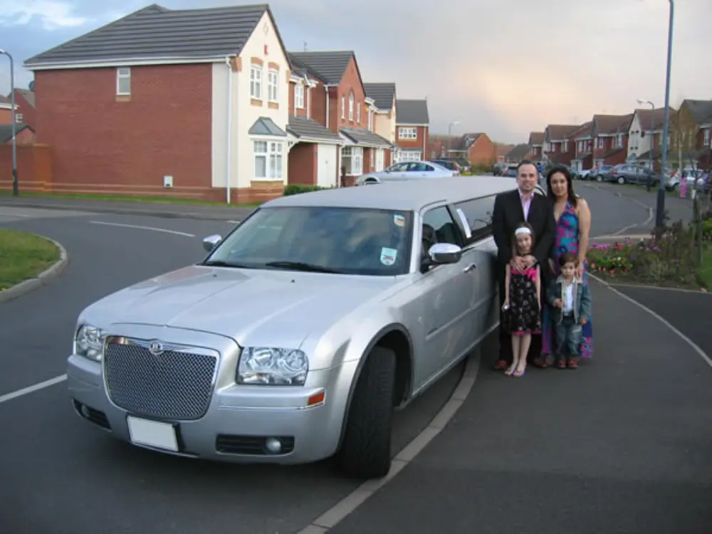 Family of four dressed in formal attire posing alongside silver Chrysler stretch limousine