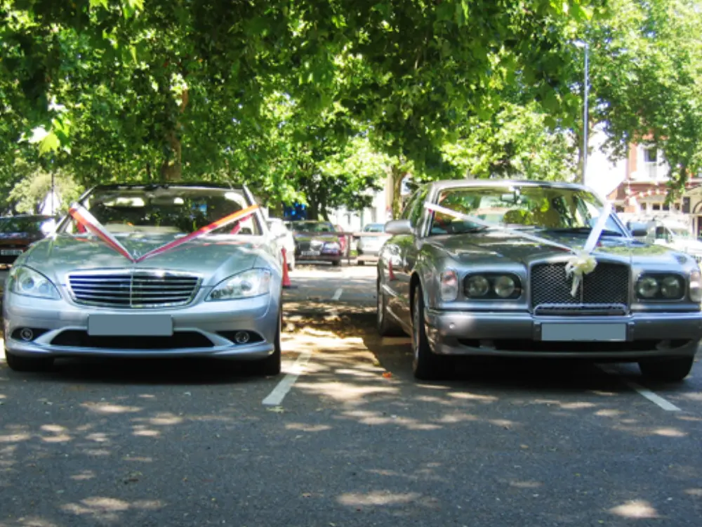 Silver Mercedes-Benz and silver Bentley wedding cars parked side by side with wedding ribbons
