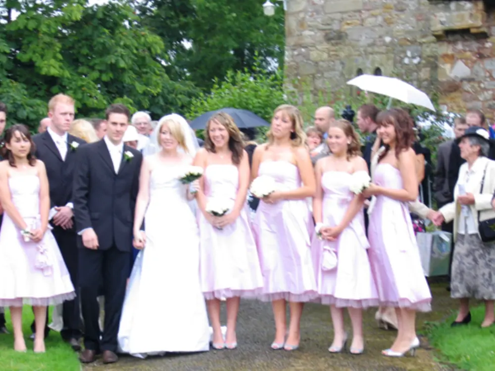 Bride and groom with five bridesmaids in pink dresses posing outside stone church