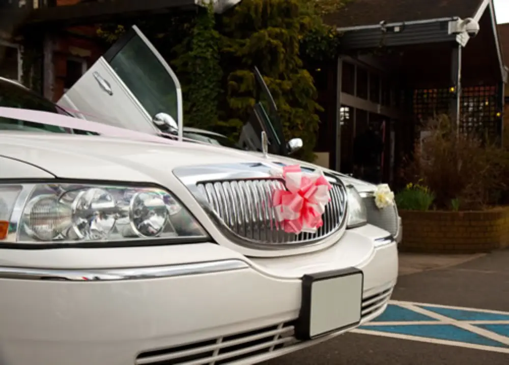 Front grille of white Lincoln stretch limousine decorated with pink wedding ribbon and bow