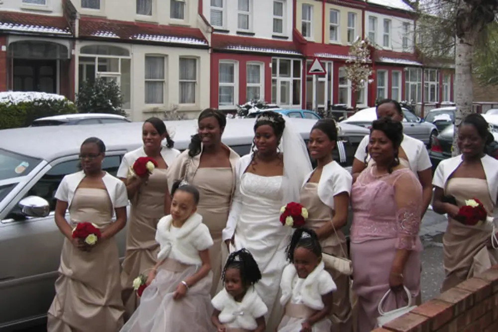 Bride, bridesmaids in champagne dresses and flower girls standing beside silver stretch limousine in winter