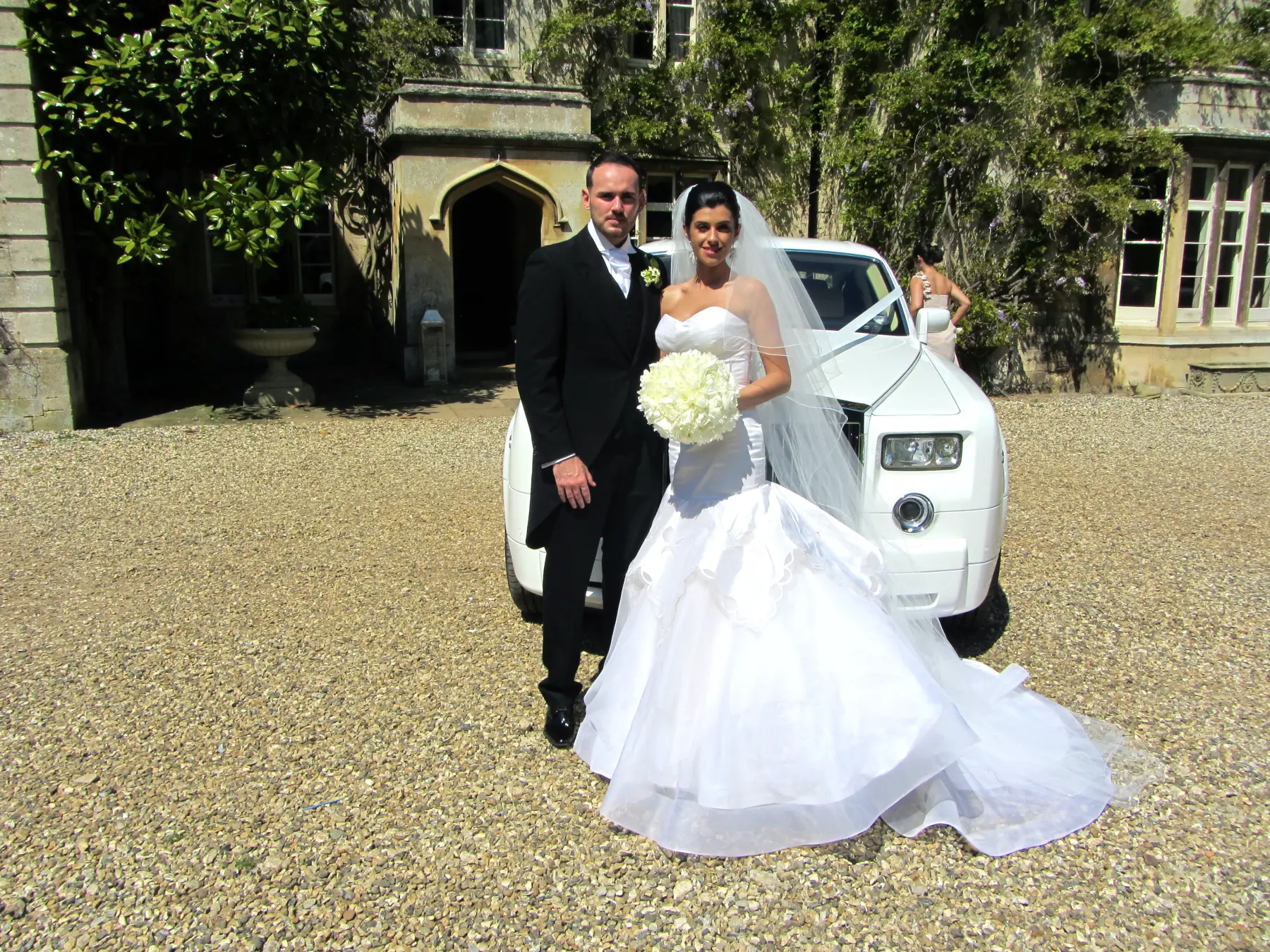 Bride and groom posing together in front of white Rolls-Royce Phantom on manor driveway