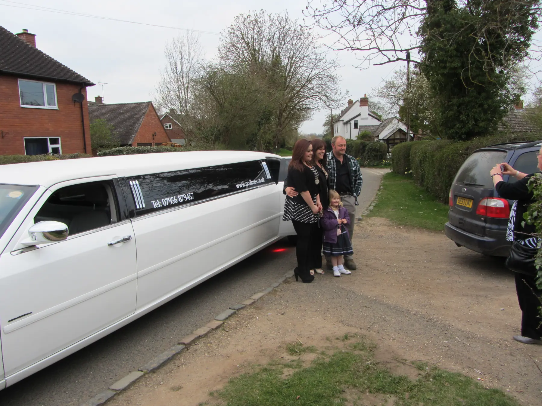 Family group posing together alongside white stretch limousine in residential setting