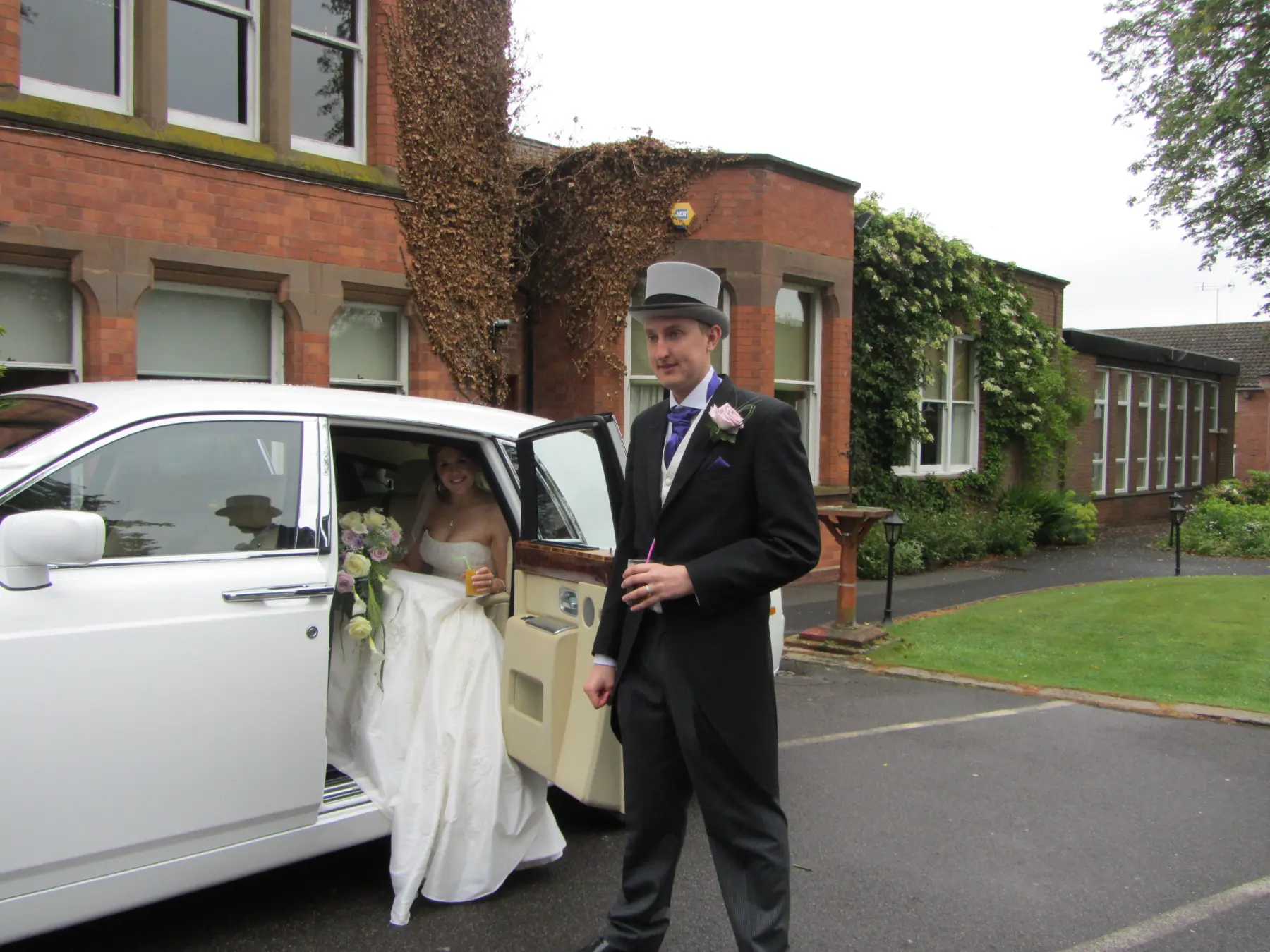 Groom in top hat and tails standing beside white Rolls-Royce Phantom with bride seated inside
