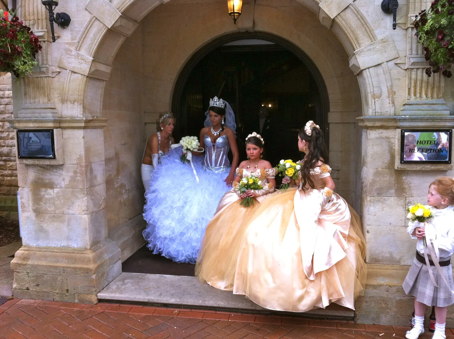 Gypsy wedding bride in large ruffled gown with bridesmaids in gold dresses at stone church entrance