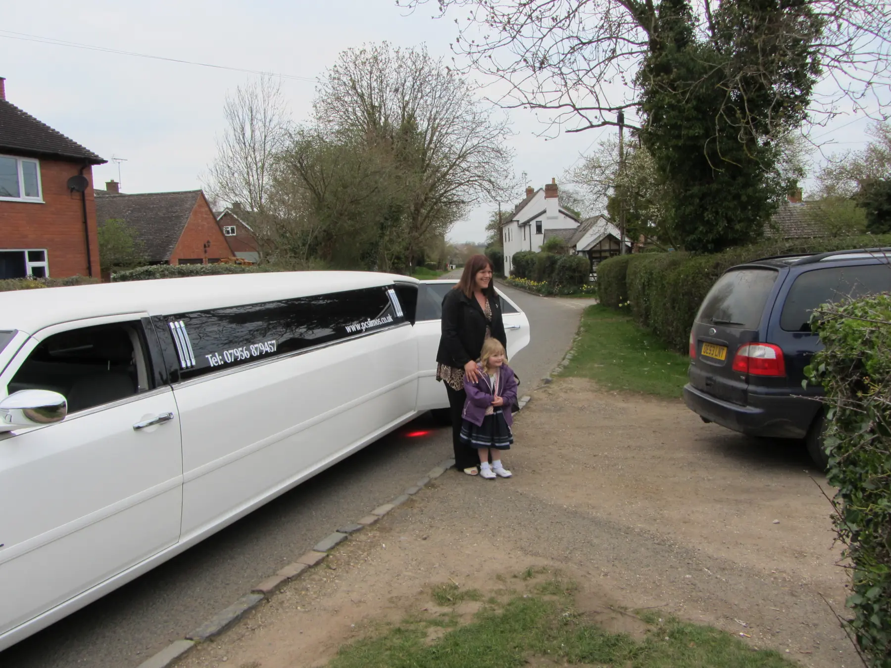 Mother and daughter posing next to white stretch limousine on rural village road