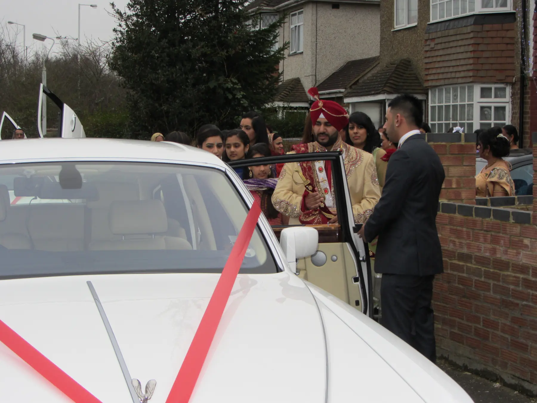 Sikh groom in ornate gold sherwani and red turban stepping out of white Rolls-Royce Phantom