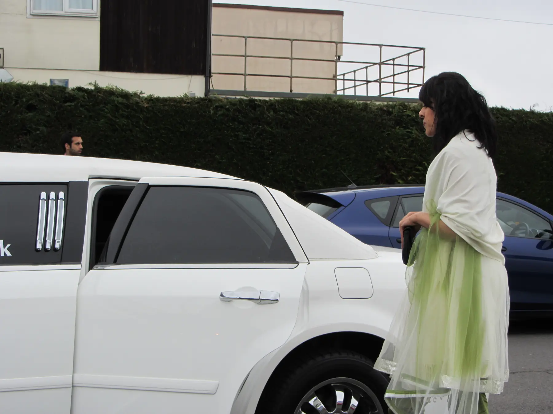 Wedding guest wearing white shawl and green dress standing next to white limousine