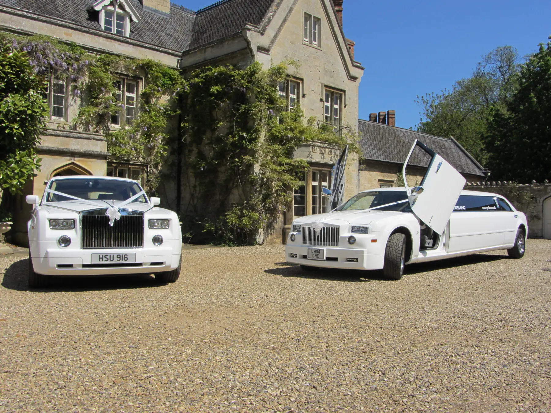 White Rolls-Royce Phantom and white scissor-door stretch limousine on sunny manor driveway