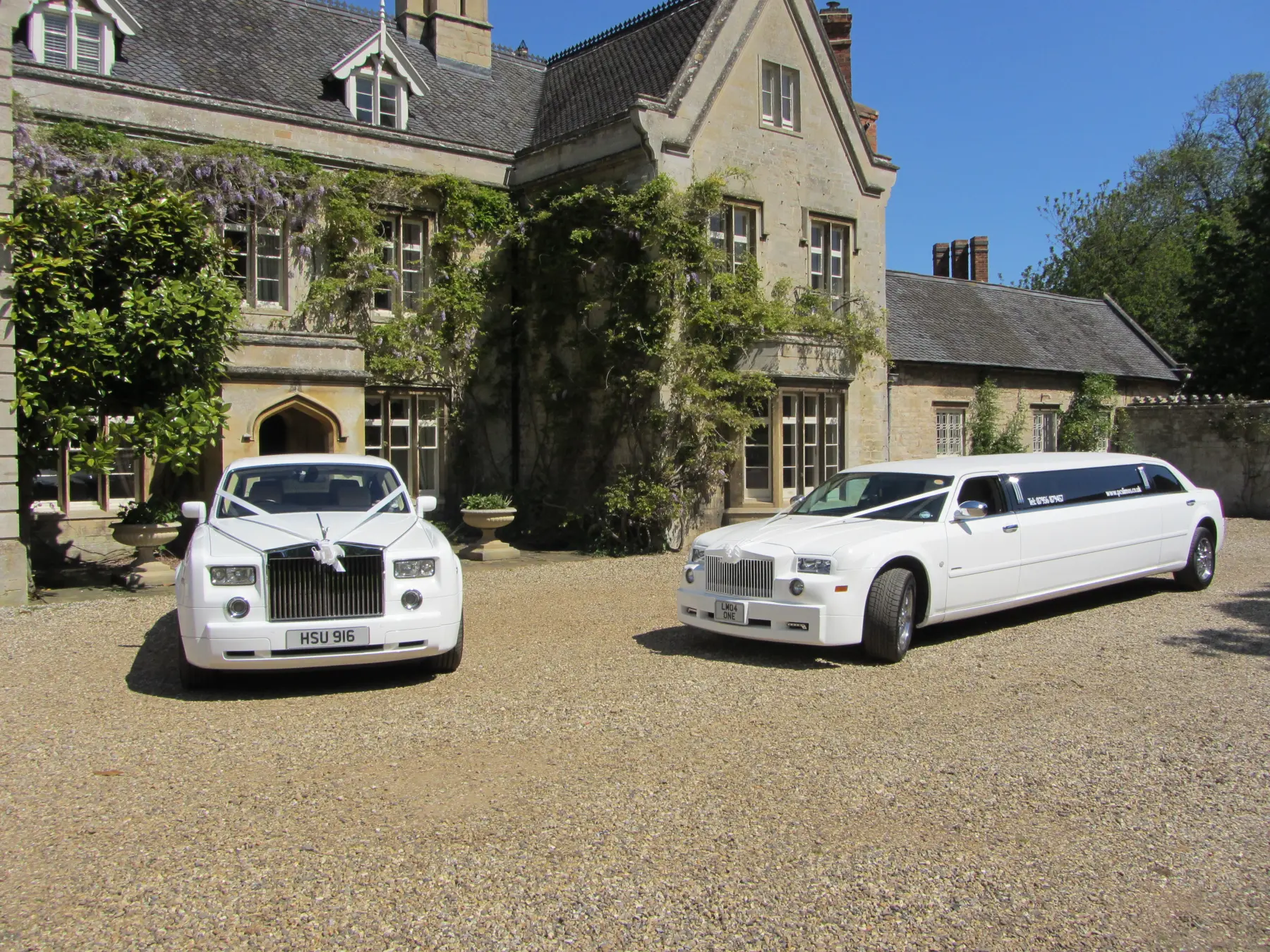 White Rolls-Royce Phantom and stretch limousine parked in gravel courtyard outside historic stone manor