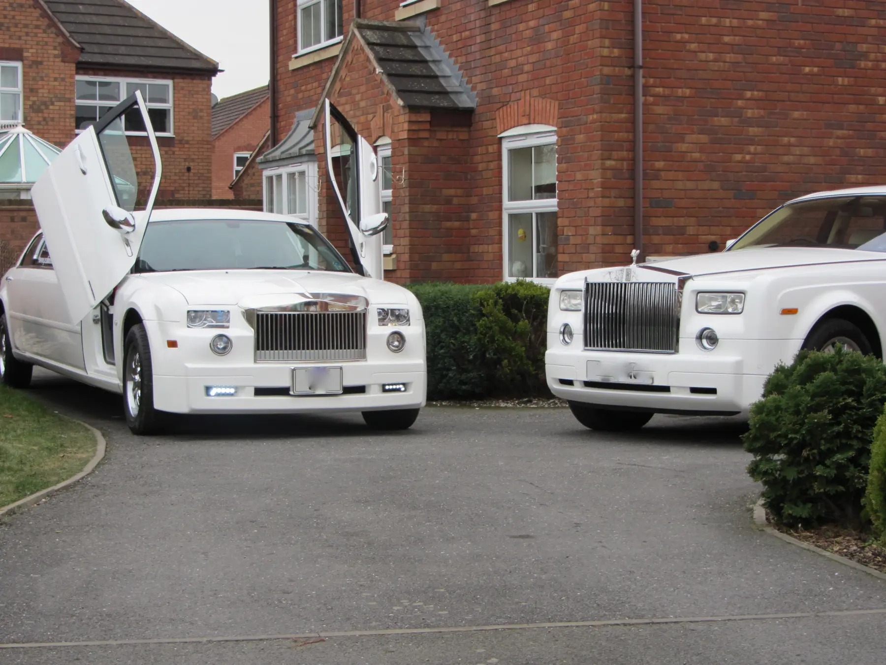 White Rolls-Royce Phantom beside white stretch limousine with open scissor doors on driveway