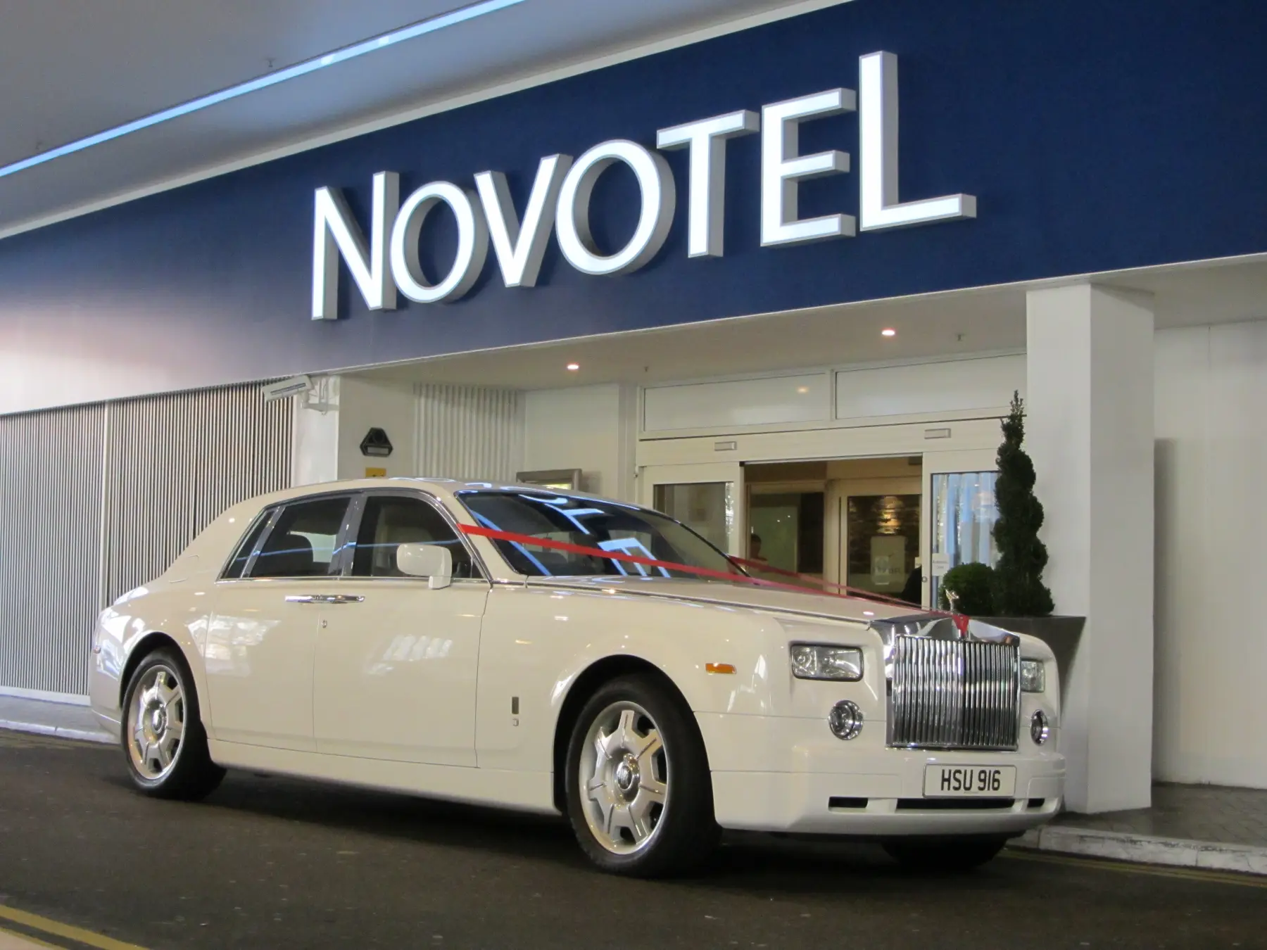 White Rolls-Royce Phantom wedding car with red ribbons parked outside hotel entrance