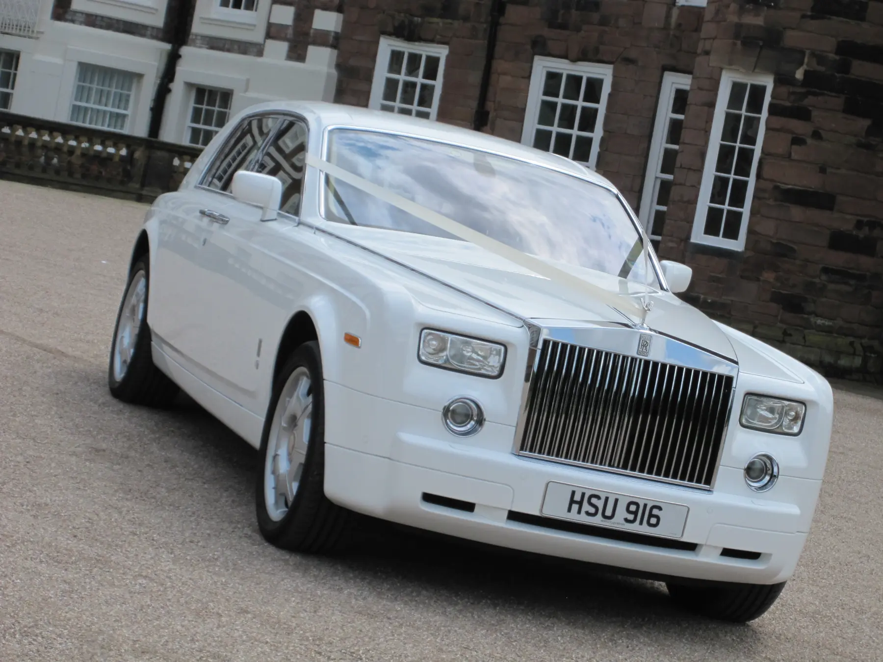 White Rolls-Royce Phantom wedding car with bonnet ribbons on gravel driveway outside manor