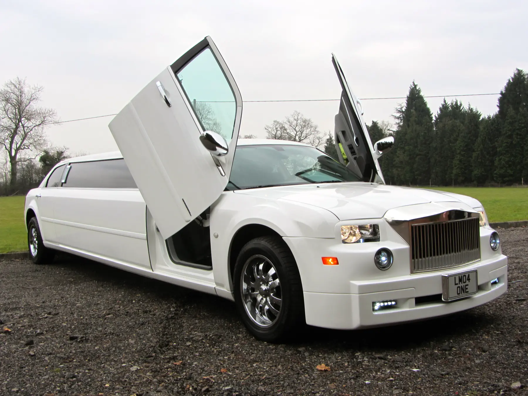 White Rolls-Royce style stretch limo with gullwing front doors open on gravel driveway