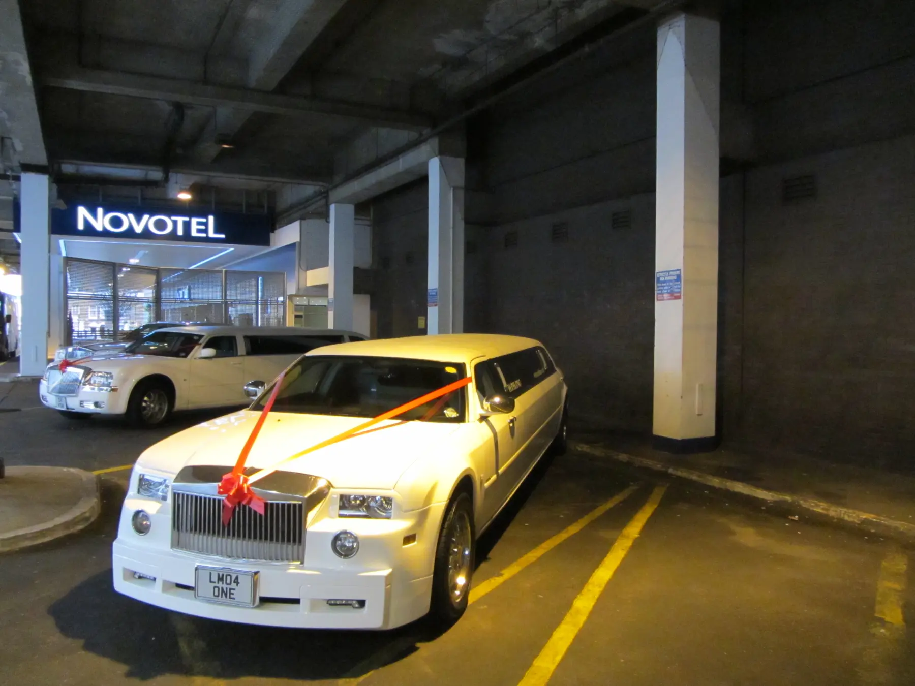 White Rolls-Royce style stretch limousine with red wedding ribbon in covered parking area