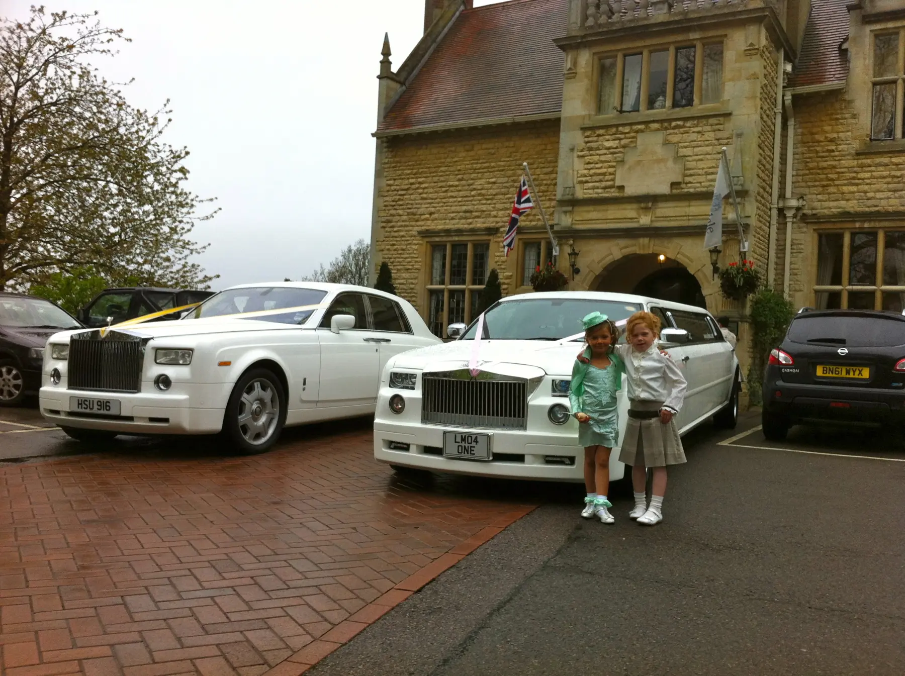 Two young flower girls in dresses standing in front of white Rolls-Royce Phantom and stretch limousine